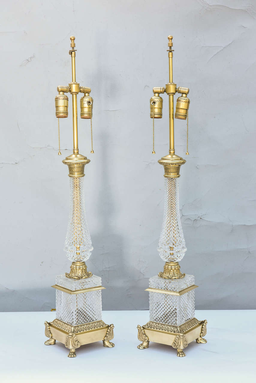 Pair of cut-crystal lamps, in Empire taste, of baluster form; having chased collars and caps of bronze dore, set upon square plinths, raised on winged paw feet. Adjustable shade-mount.