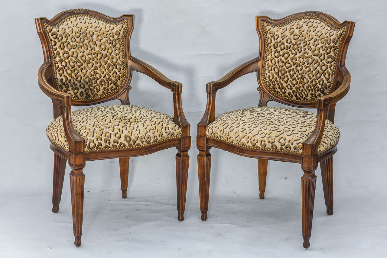 Pair of Louis XVI style fauteuils, of walnut, each with a padded shield-form back, surmounted by a molded crest, joined by padded scrolling arms, to its crown seat, raised on fluted, tapering square legs ending in spade feet. Upholstered in