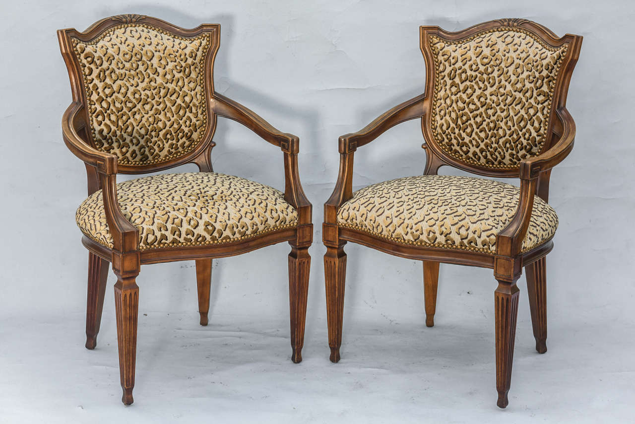 Paire de fauteuils de style Louis XVI, en noyer, chacun avec un dossier rembourré en forme de bouclier, surmonté d'une crête moulurée, relié par des bras défilants rembourrés, à son siège en couronne, le tout reposant sur des pieds carrés cannelés