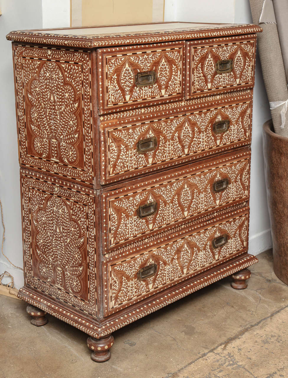 A tall chest of drawers with bone inlay in a Classic pattern, from India. Five drawers with brass pulls. Two sections, bun and post feet, marble inset top.