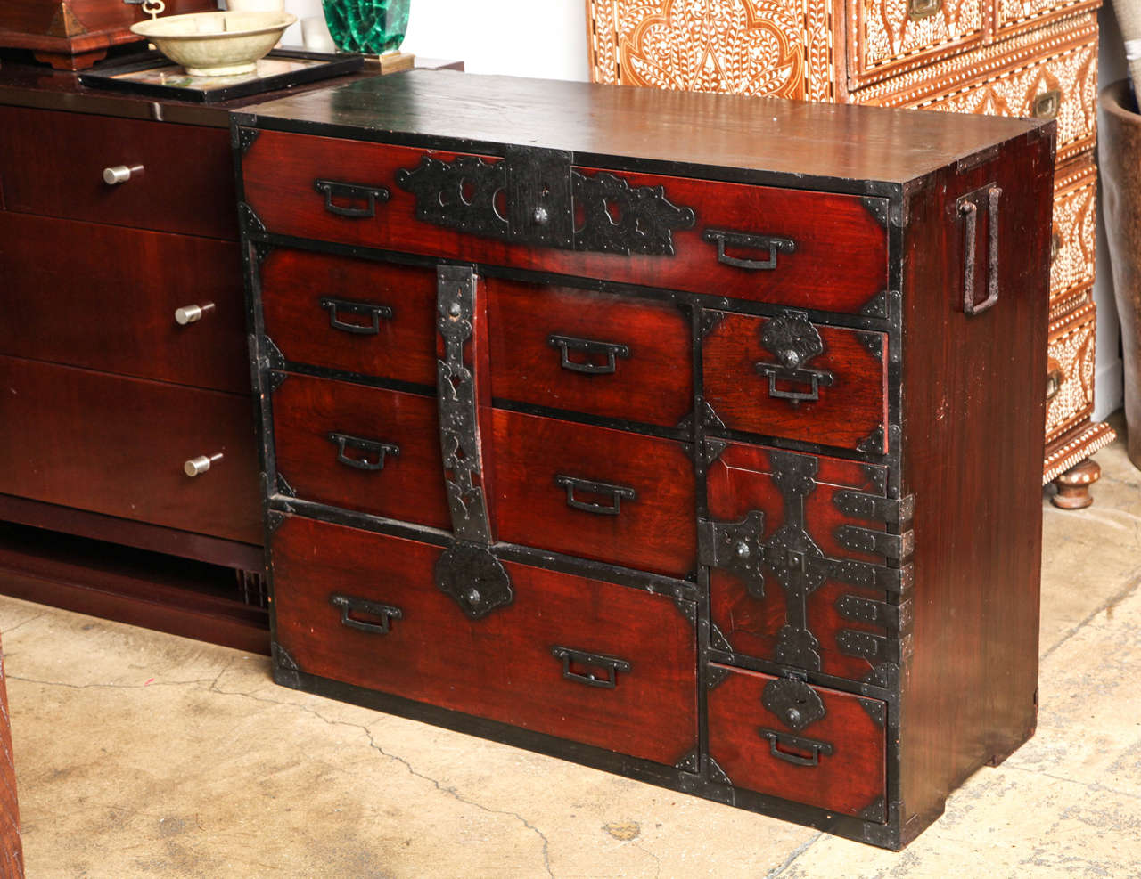 A Japanese Tansu cabinet or chest in dark finish, with metal trim and pulls and hinges. Hidden drawers behind door. Vertical brace secures middle drawers. Meiji period.