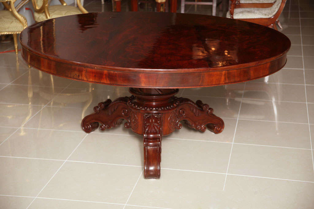 The flame mahogany top above a pedestal with elaborate carving, beading, rosettes, resting on three carved legs with similar motifs.