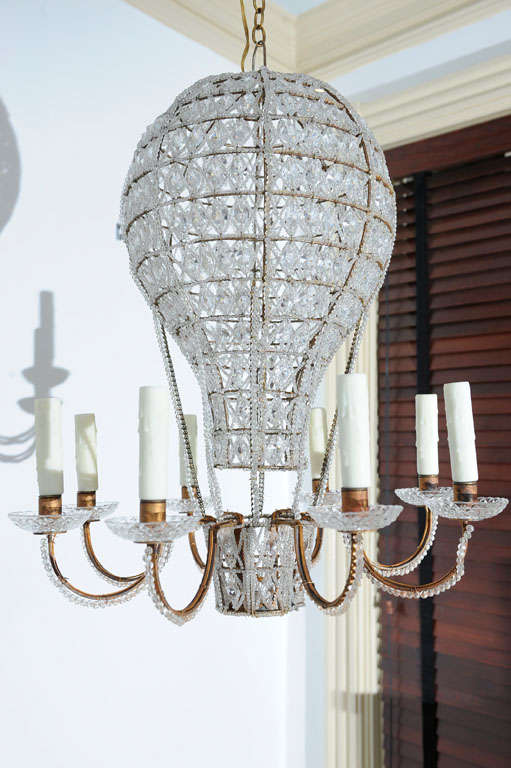 This unusual fixture will be a conversation piece in any room.  A delicate metal frame is covered with crystal string beadwork, while open spaces are filled with crystal octagons. Eight candle arms extend from the passenger basket at the base of the