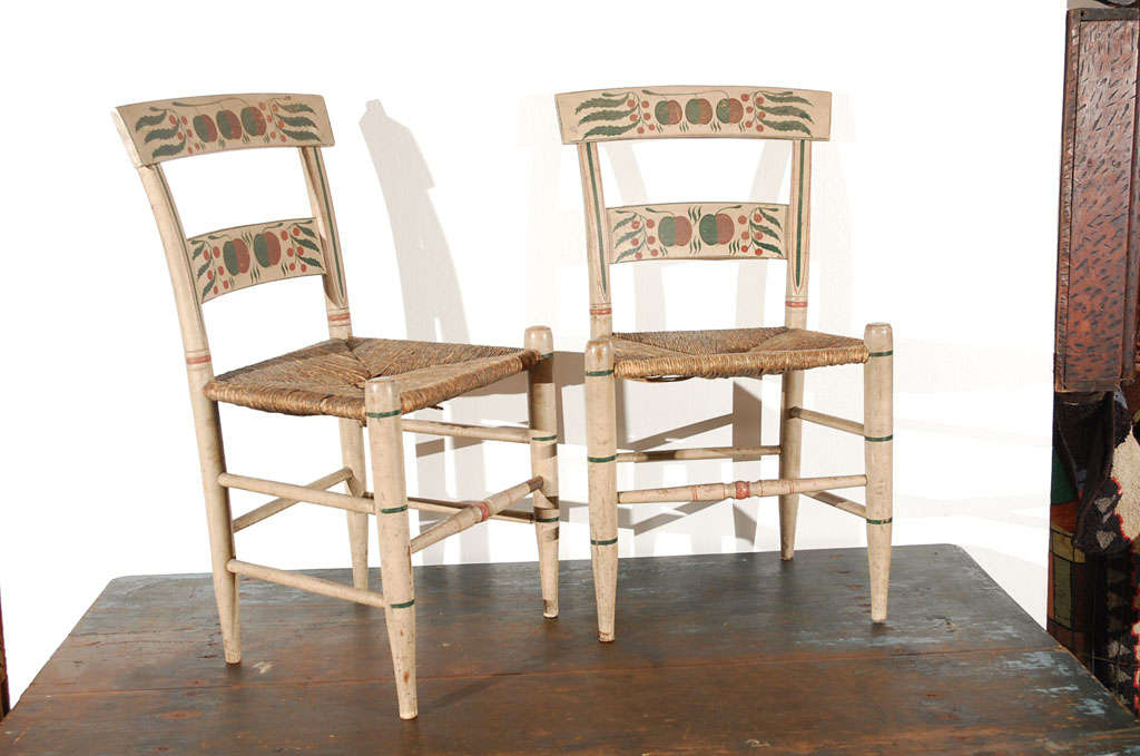 RARE FANCY ORIGINAL 19THC PAINT DECORATED PAIR OF CHAIRS FROM NEW ENGLAND.THIS FANTASTIC PAIR OF PAINT DECORATED CHAIRS  HAVE CHERRIES ON BOTH BACKSPLASH PANELS AND SPINDLES ARE DECORATED WITH RED AND GREEN STRIPES.THE SEATS ARE ORIGINAL RUSH SEATS