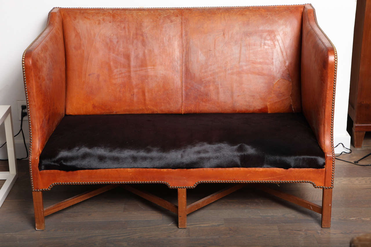 A rare and wonderful loveseat by Kaare Klint. Original leather, repaired in some places , with great character and color. 
The seat has been replaced with a hair-on cowhide in chocolate brown. The lower edges, arms and back are finished with