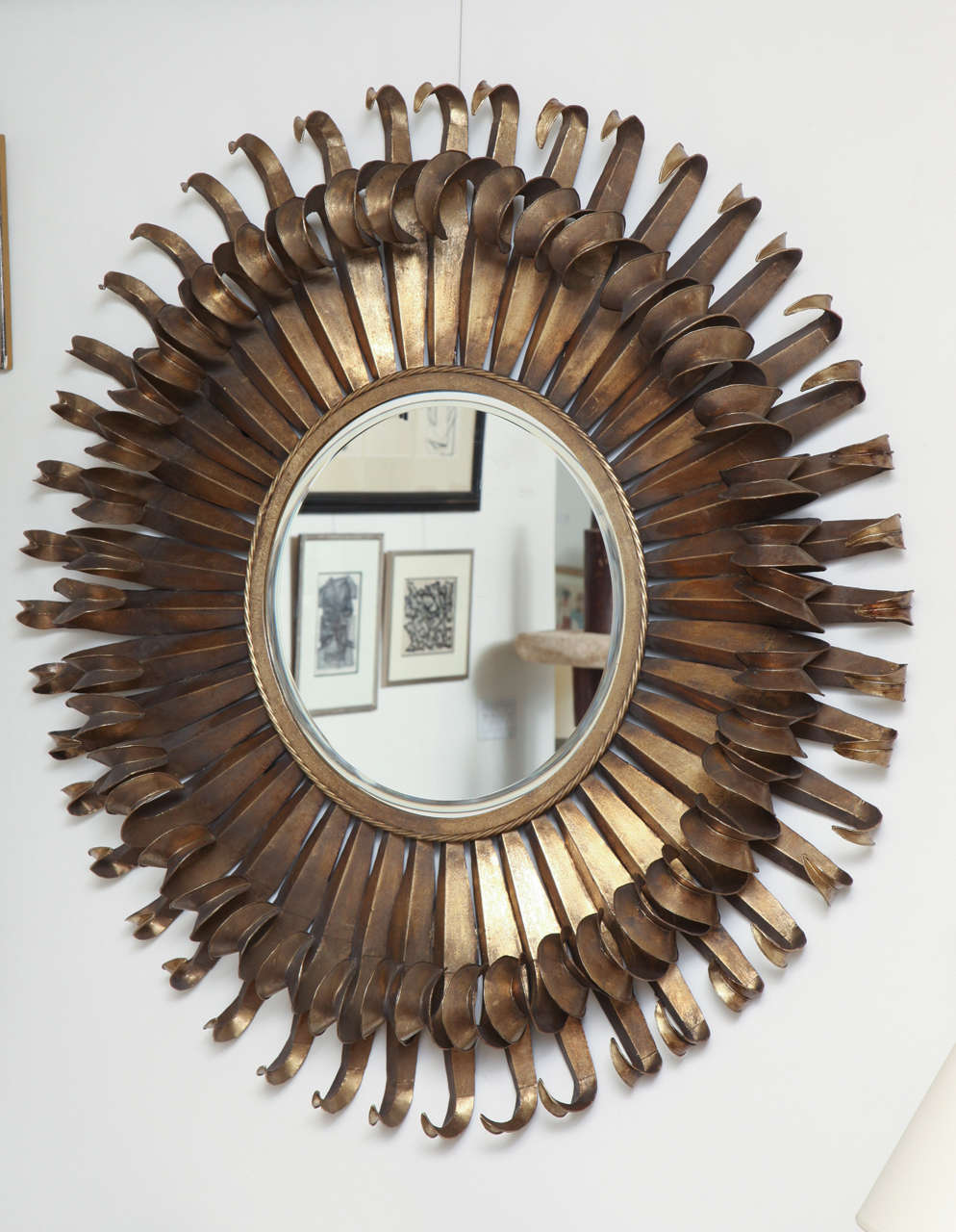 Round gilt iron mirror made of two layers of curled patinated metal in a sunburst style with central beveled mirror