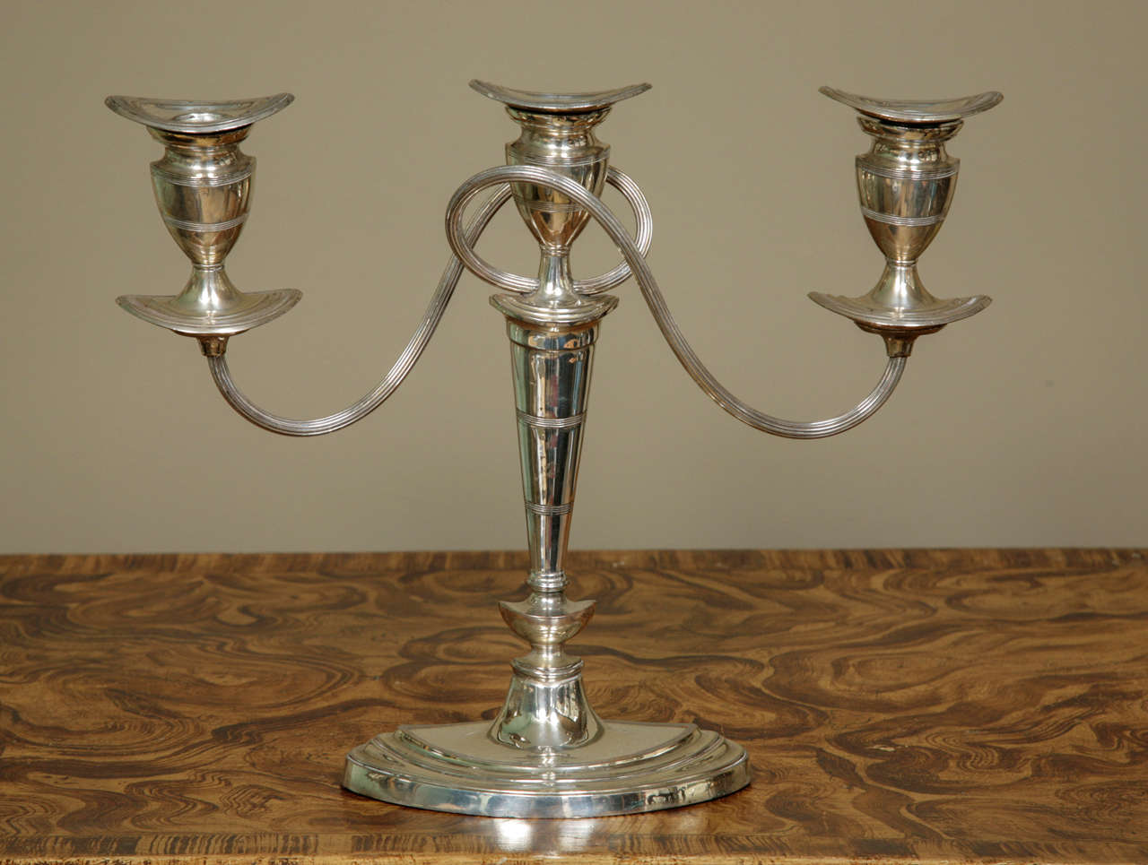A stylish pair of Georgian Sheffield silver plated triple candle pair of candelabra in a very elegant Neoclassical style. The urn-shaped finials have removable drip pans  and are supported by ridged double swirl arms. This pair date from ca. 1790.
