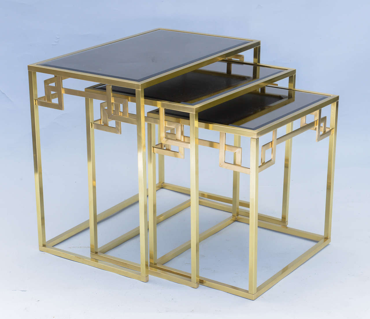 Set of three tables, in graduating size, of polished brass, each having a smoked glass top, on pierced apron with stylized Greek key corners, raised on square boxed-frame legs.

The medium table is 20.5