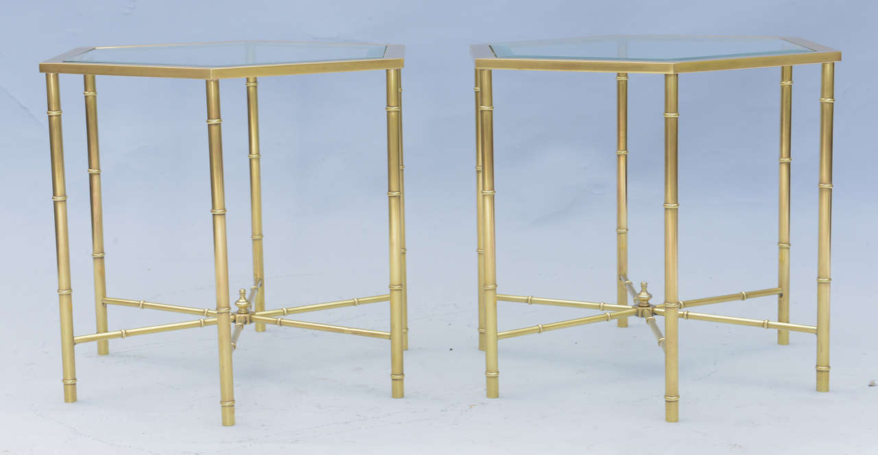 Pair of end or side tables, of polished brass, each having beveled hexagonal glass tops, raised on six stylized-bamboo form legs, joined by star stretcher, centered with a finial.