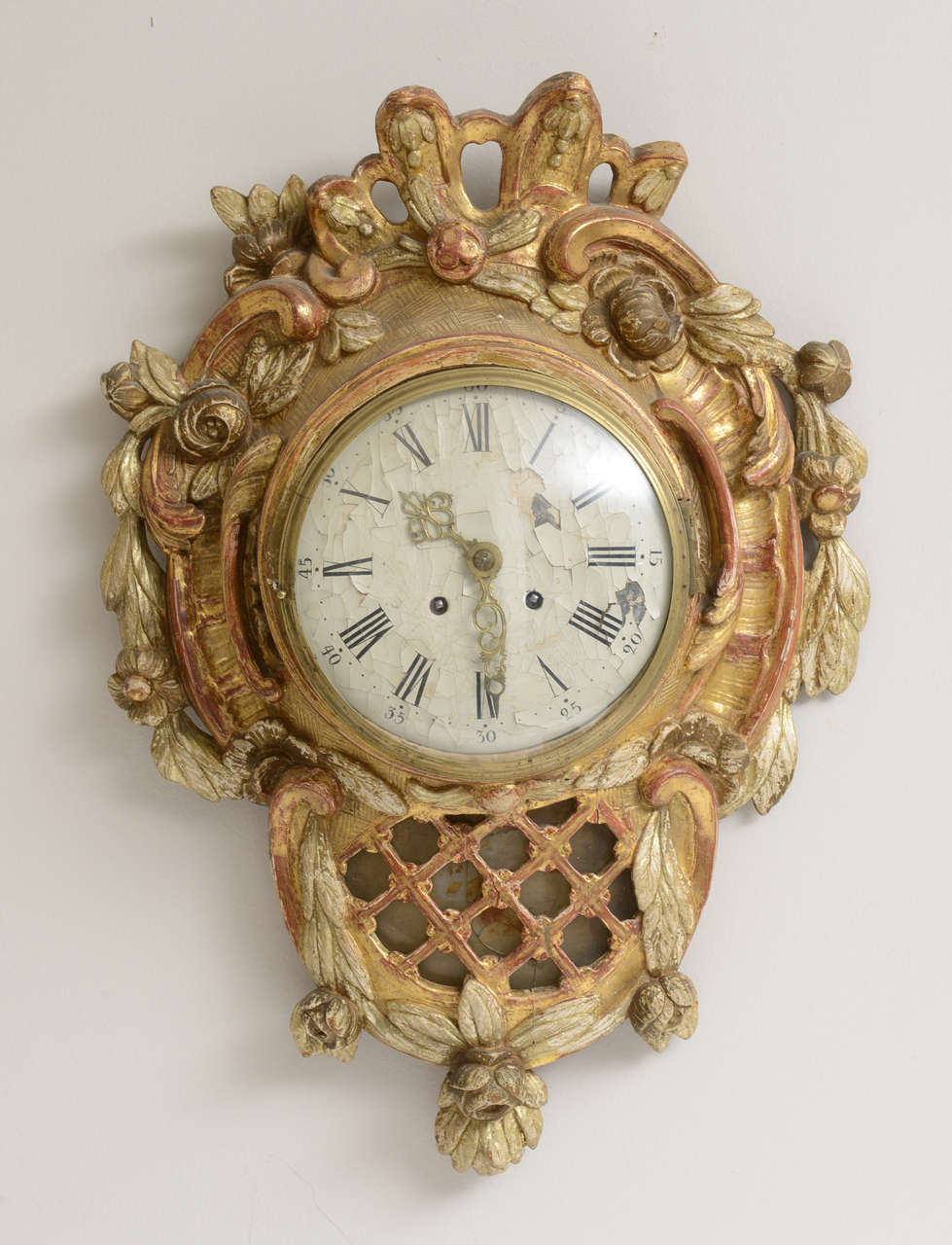 Swedish Giltwood Wall Clock from the late 18th/early 19th century. Circular face is enclosed in bellflower, lattice and foliage carved frame. The glass cover of the face opens. The background on the numerical face has some paint loss and heavy