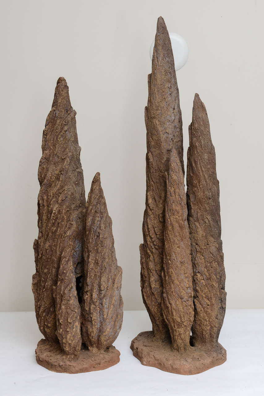 Pair of French early 1900's sculptures of cypress trees made of brown porous terra cotta. Each sculpture represents a group of three cypress trees on a thick base. The sculptures are not identical - one is 40