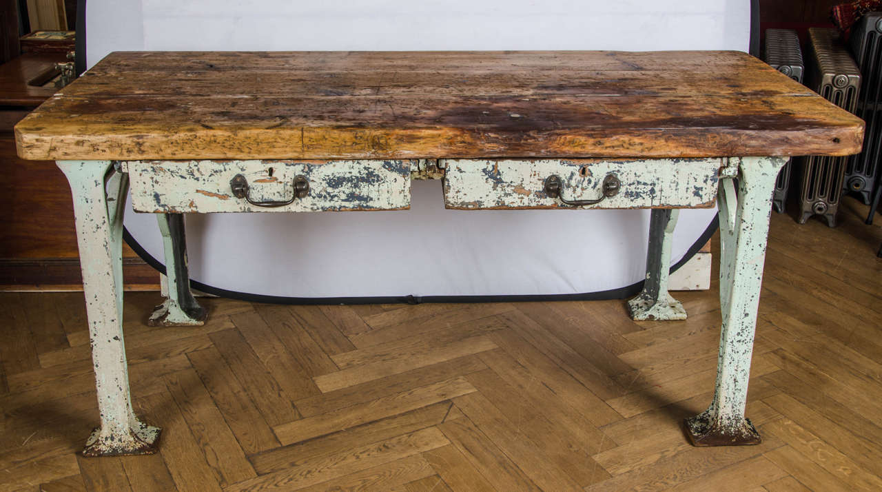 A large rustic table with a cast iron base and thick timber top. This substantial vintage industrial table has a characterful cast iron base with utility style arched legs and a thick, worn pine top. The table has two compartmentalised drawers with