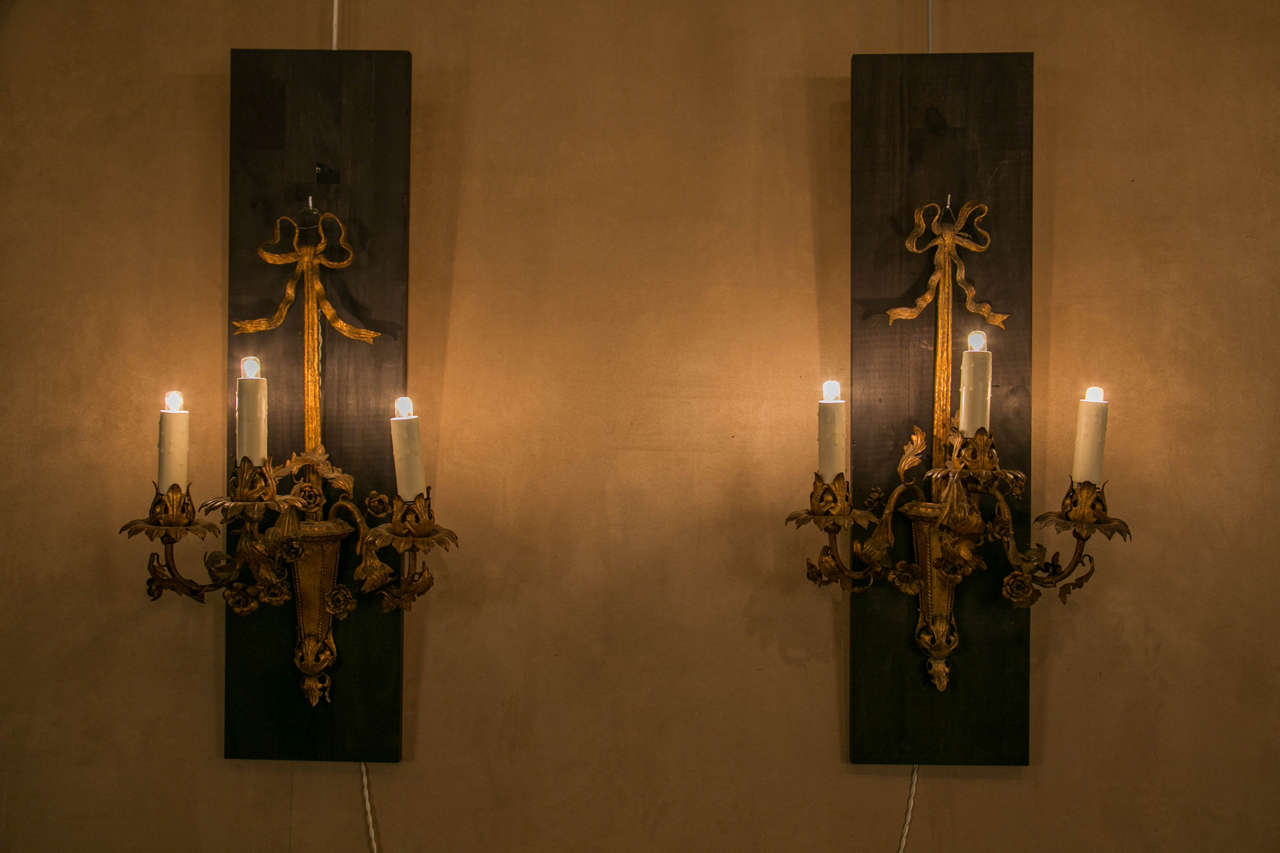 Pair of gilt metal wall sconces, decorated with flowers on the arms.
Each sconce features a carved ribbon on top and carved laurel leaves on its bottom section.
In the spirit of Maison Baguès.