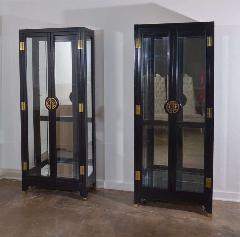 Pair of black American of Martinsville display cabinets with brass accent hinges and handles. Mirrored back, beveled glass doors, four glass shelves in each cabinet. They are lit and in working condition.