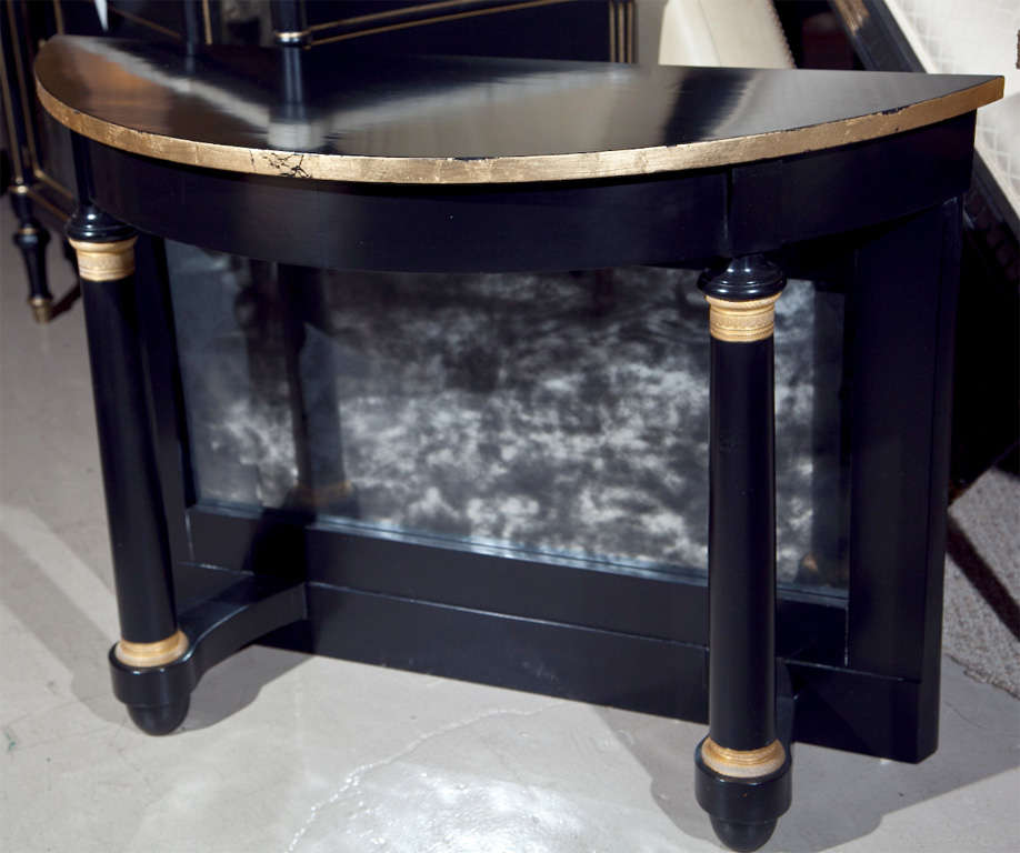 Pair of decorative ebonized pier demilune tables, 20th century, the half-moon top supported by two columnar uprights, decorated by a mirror veneered back splat. One mirrored panel broken. In need of replacement mirrors. As is price on Sale.