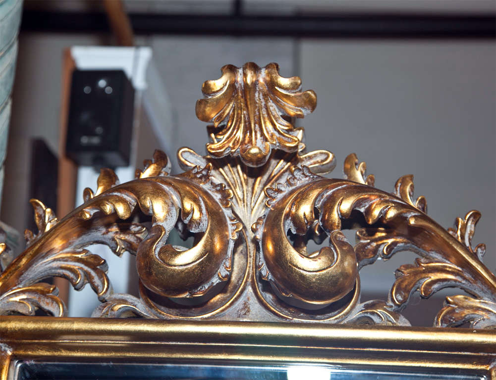 Pair of elegant French Baroque style giltwood floor mirrors on trestle bases, circa 1940s, each with simple rectangular frame surmounted by intricate carving of scrolls and foliage.