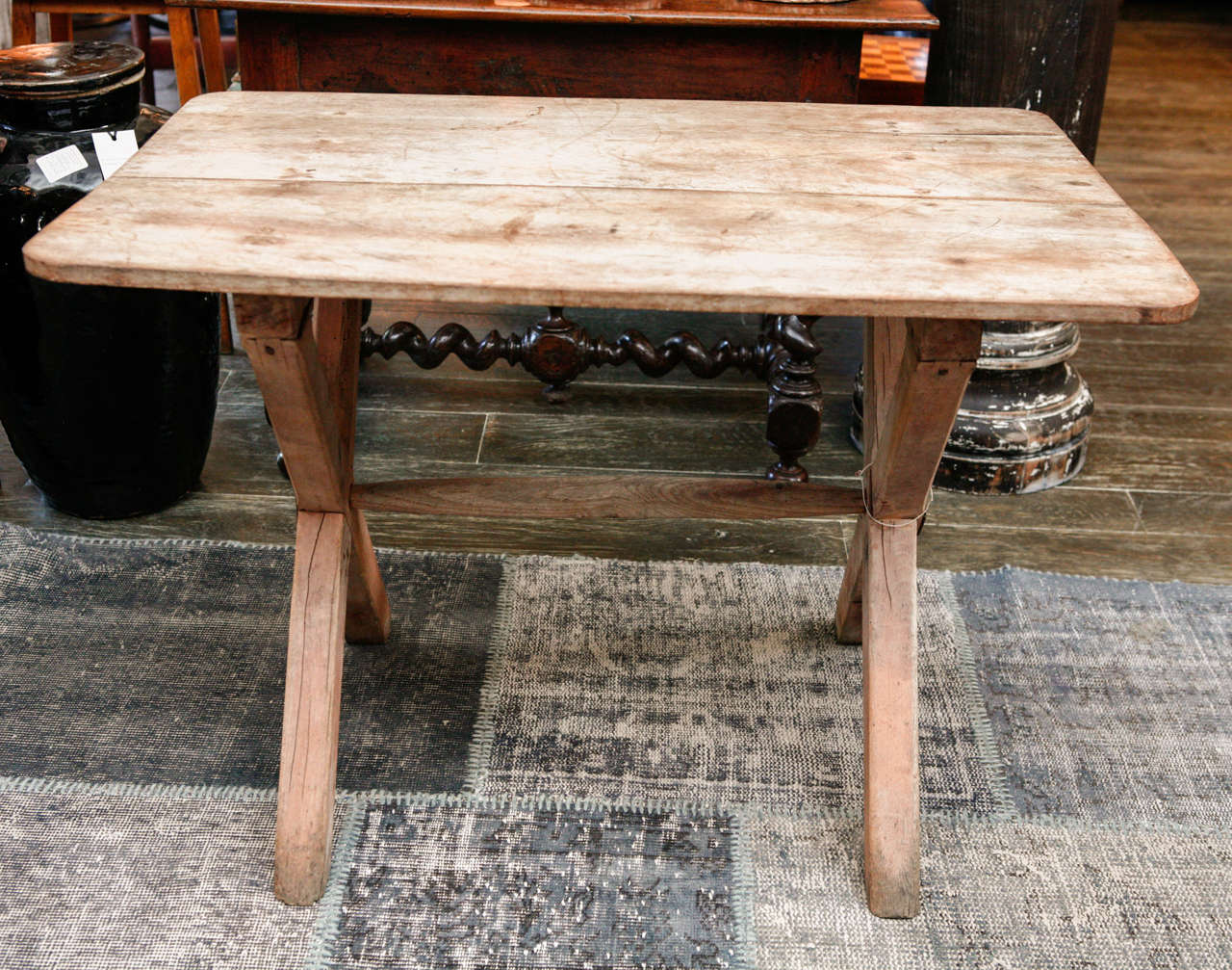A bleached wood table with x-legs joined by a center stretcher