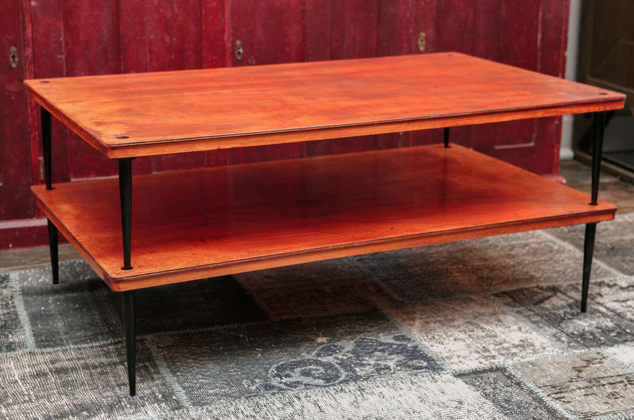 A coffee table with two rectangular molded edge table tiers supported by tapering painted metal legs.