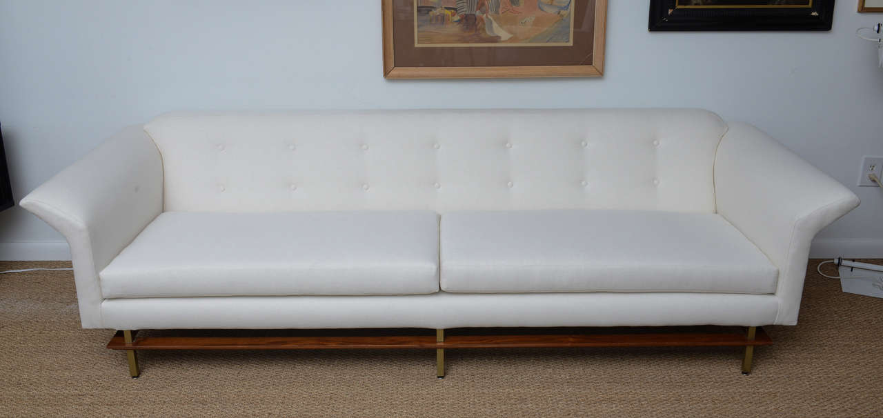 Long sofa with square brass legs interconnected with wrap around walnut frame. Newly upholstered in cream duck cloth simple to show the lines---can easily be upholstered in the fabric of your choice.