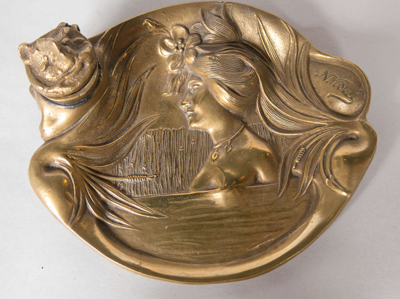 20th century brass inkwell, signed Novidal. Descriptive woman carved on to a floral landscape.
