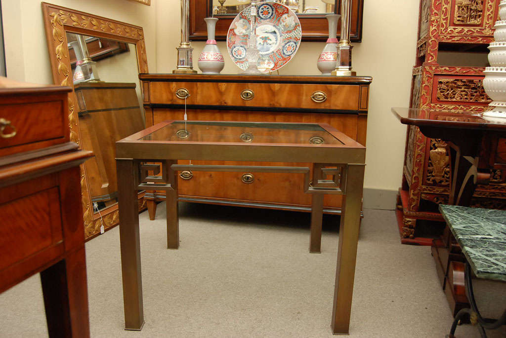 Patinated brass base table with greek key design and glass top.