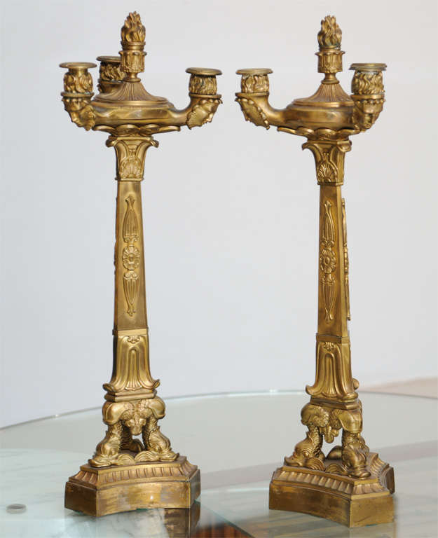 The central flame finial with three candle cups with masks over a central stem with acanthus over a tripartite base with dolphin heads.