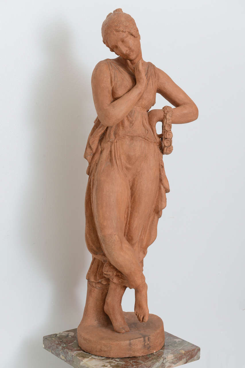This charming sculpture dates from the early part of the 19th century in France. Here we have a young girl dressed in a sensual, flowing gauzy-garment with a floral-ring around her arm as she seems to contemplate or perhaps plan a moment of love and