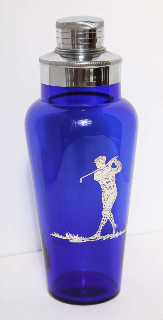 A wonderfully handsome Art Deco American made blue glass and Sterling silver applied golf scene cocktail shaker.  
The lid is a two piece removable lid made of silver plate, and allows the top cap to be removed to strain drinks through.
The
