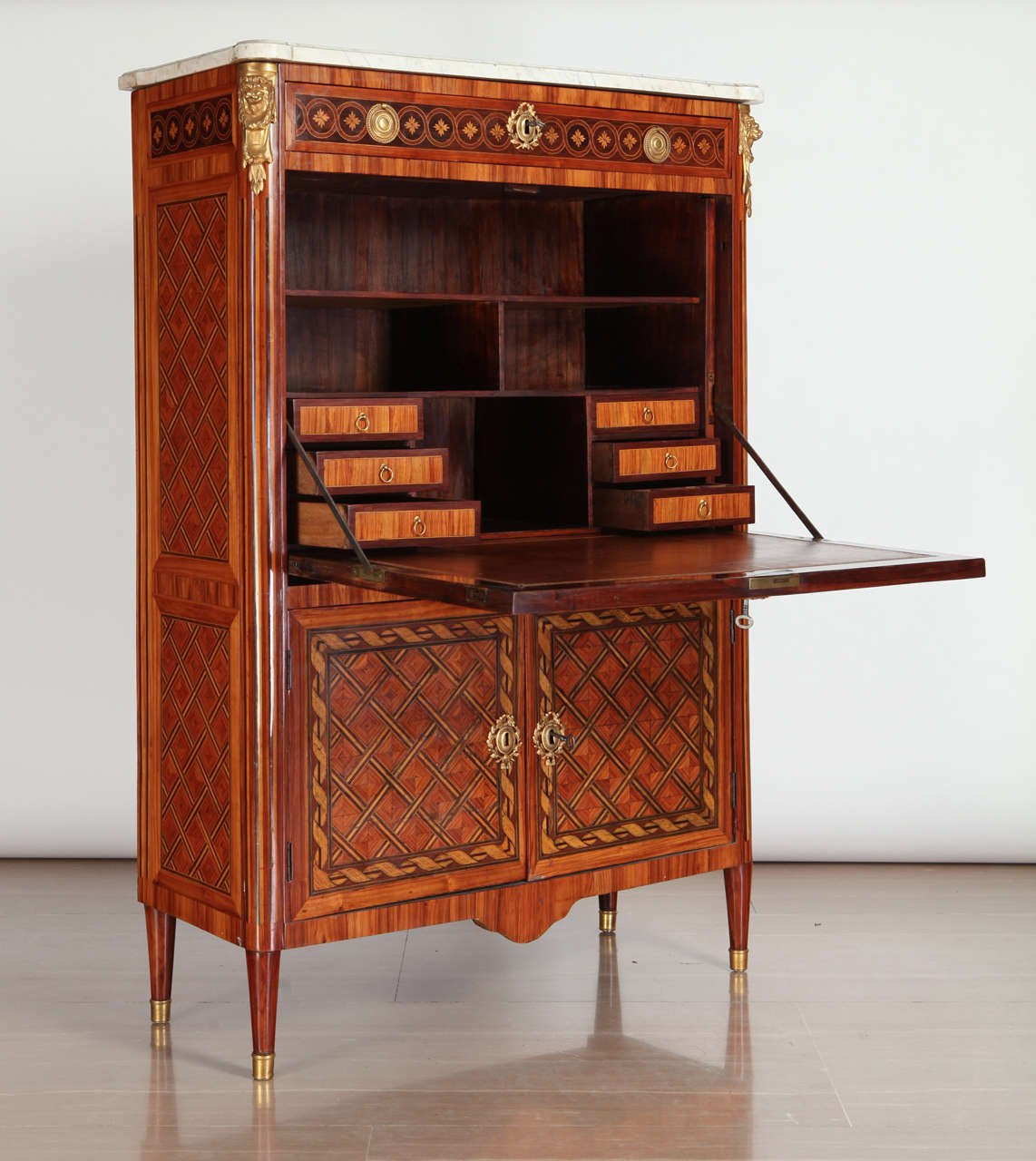 Fino secretaire abattant francés de marquetería y parquetería de kingwood, tulipwood y sicomoro teñido, montado en ormolina, con tapa rectangular de mármol blanco moldeado, sobre un cajón de friso con incrustaciones de cabezas de flores, frente de