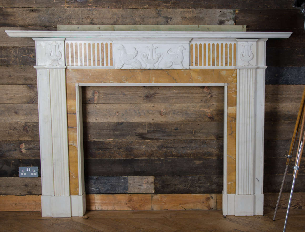 An attractive English Georgian style surround with contrasting Sienna marble inlay. This fireplace surround features a carved marble central plaque featuring two Griffins flanking a stylised lute motif, which is repeated on each endblock. The