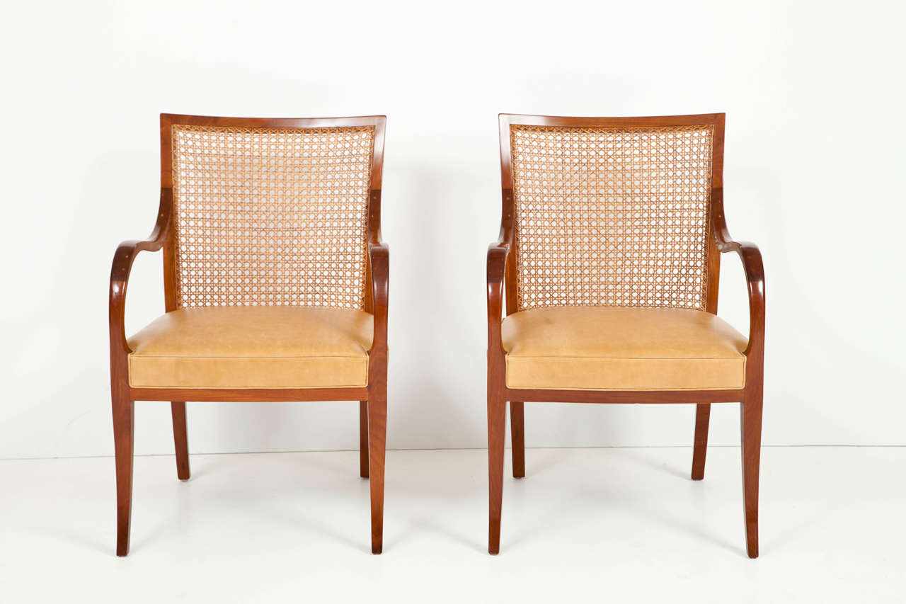 A pair of Frits Henningsen solid mahogany and French cane openchairs, Circa 1930s, eached with a rectangular caned backrest, generous scrolled armrests, a tight leather upholstered seat raised on sabre legs.