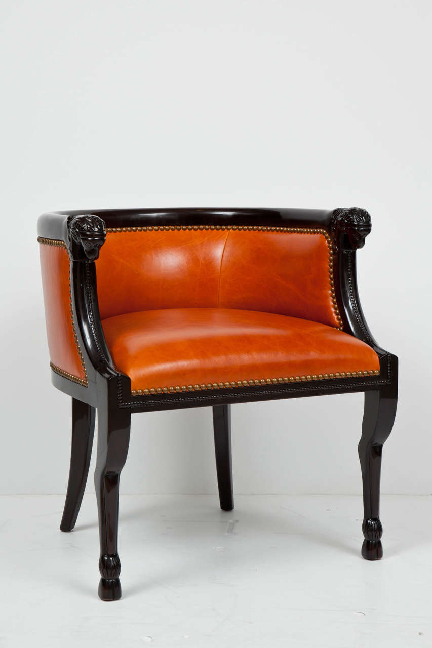 Ultra chic pair of burnt orange leather club chairs with carved, dark brown stained solid Walnut ram heads at arms and cloven front feet. Bronze nail head application finish off these tailored stately pair.