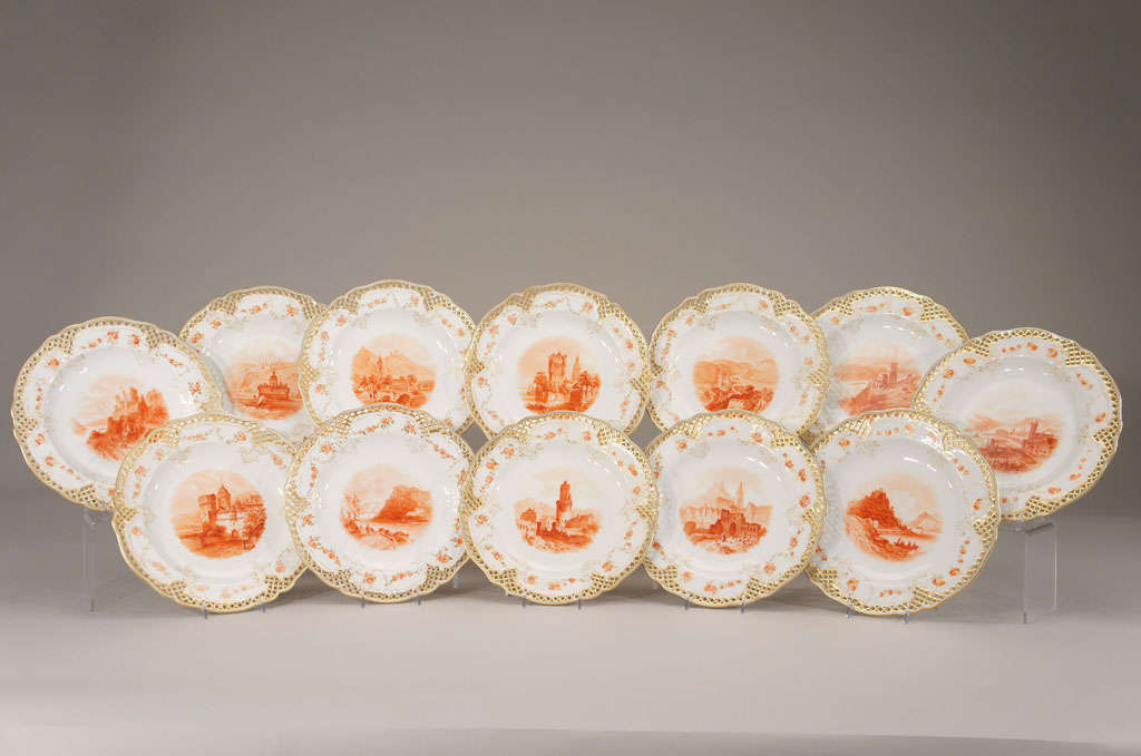 12 superbly hand painted cabinet plates with scenes of named places in monochromatic bittersweet red with pierced rims. The gold borders and molded raised flower decoration further embellish these masterful works of art. The detail and quality of