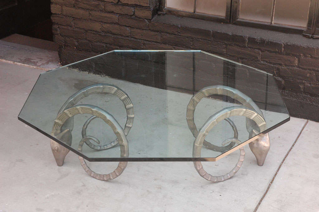 Oversized octagon glass coffee table supported by a pair of steel  ibex ram heads.