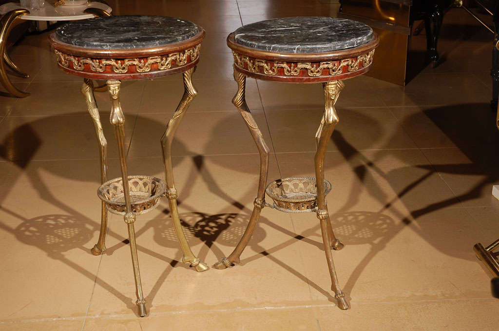 Pair of Gueirdon side tables featuring bronzed iron, female figure legs with hoof foot, inset black marble tops, and ornate gilt trim detailing.