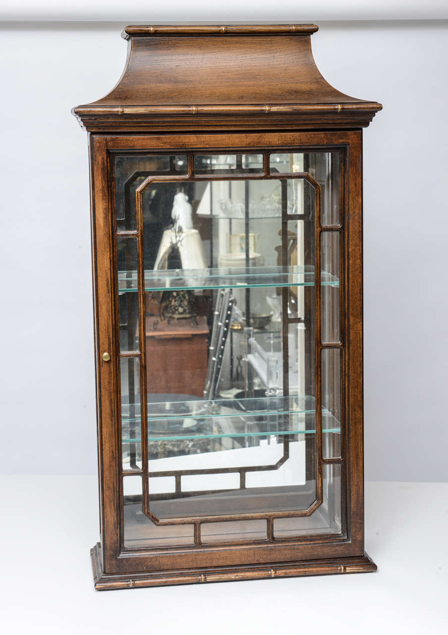Chic pair of pagoda style faux bamboo display cabinets with three sides of glass and a mirrored back.