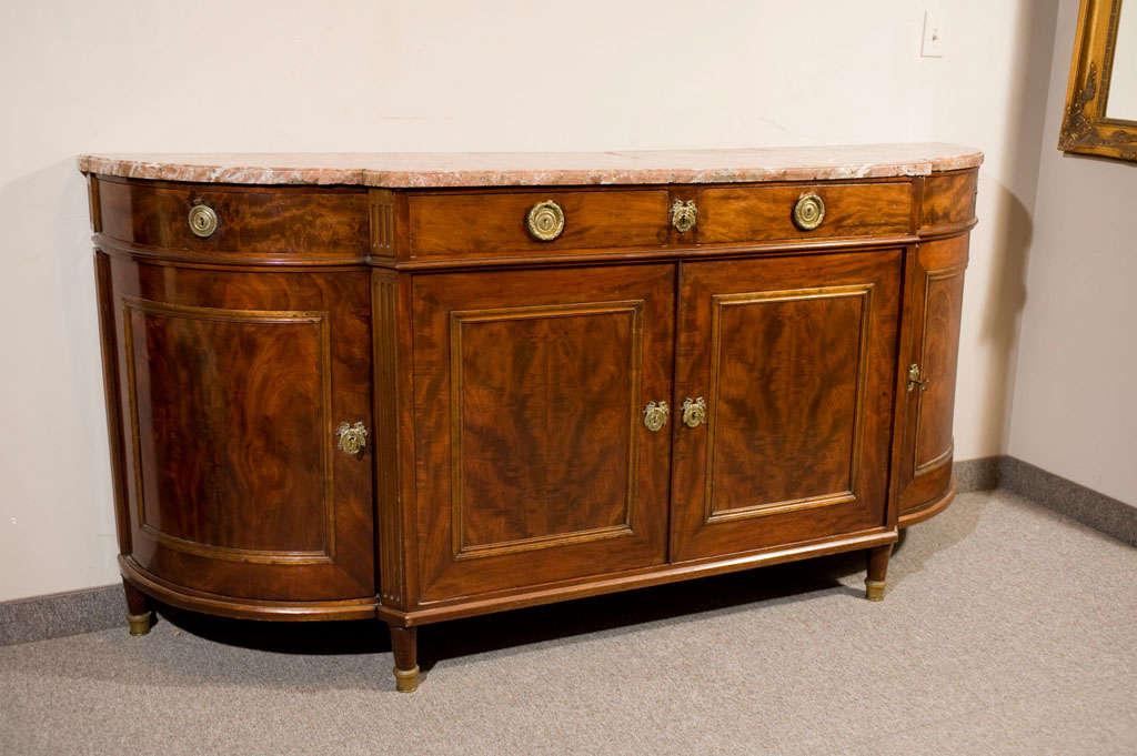 This antique marble top sideboard was made roughly in 1915. It is American-made but designed with inspiration from France. It is in its original condition and is simply stunning. It has solid brass hardware and is solid rosewood. The marble is