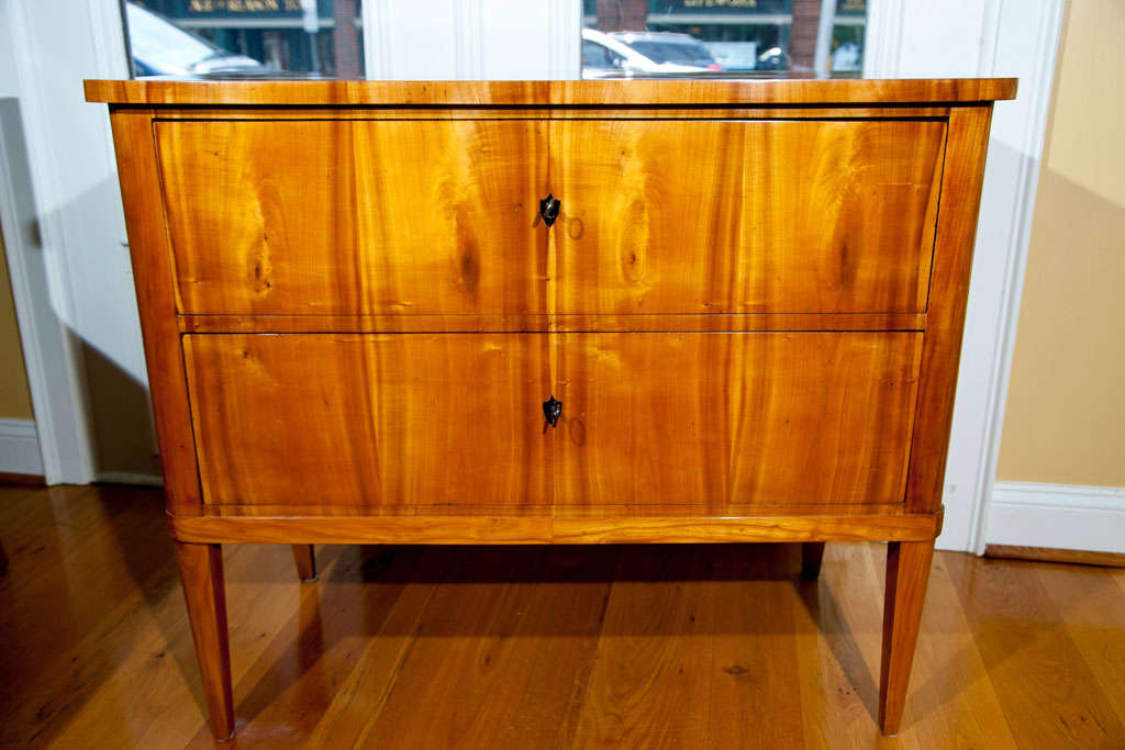 Wonderful streamline Biedermeier blonde cherry wood two-drawer chest with rounded edges finishing on straight and tapered legs, shown with ebonized shield keyholes