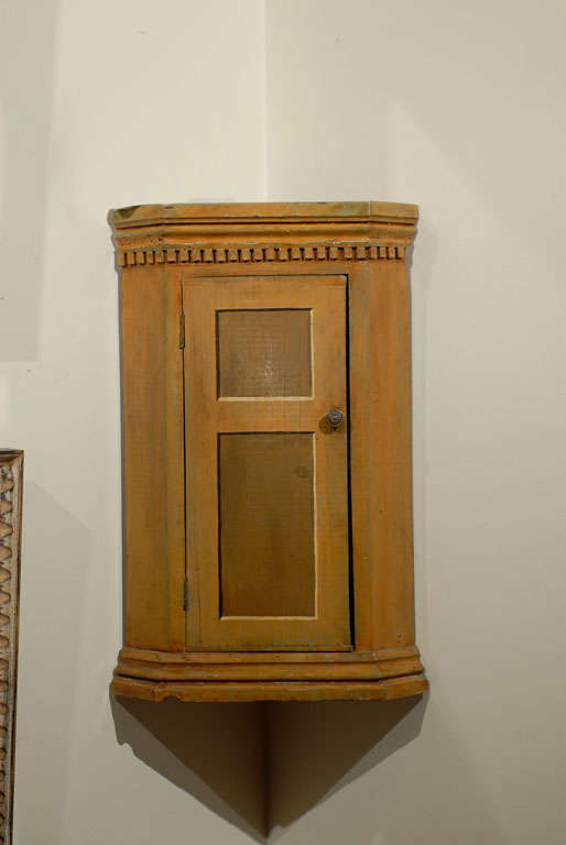 This is a wonderful little painted hanging cabinet.  The vernacular piece was designed for a specific spot.  The paint is original and very handsome.  The door is faux painted giving it a look of true panelling.  The crown molding with dentil