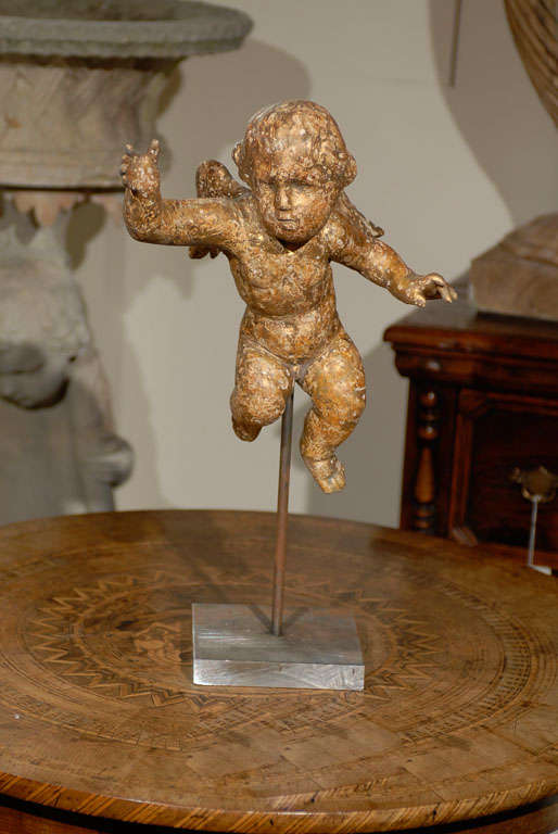 An English carved and giltwood flying cherub from the mid-19 century on metal stand and Lucite base. In a manner that an Italian Baroque sculptor such as Bernini would have approved, we are catching this English carved putto mid-flight, frozen into