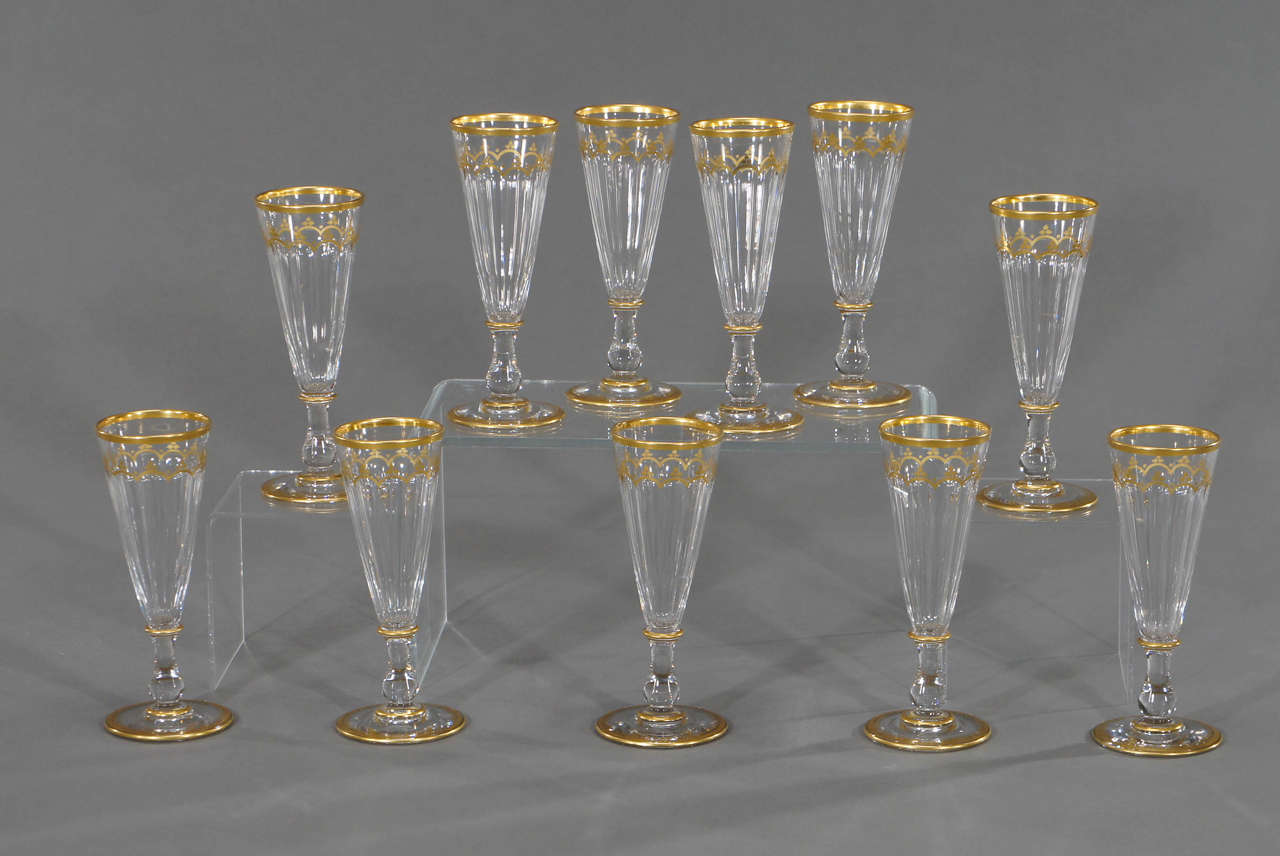 An elegant set of 11 champagne flutes that are sure to please any champagne lover. Handblown crystal with panel cutting and embellished with gold enamel decoration in the style of Harcourt services. The Fine detailed trim elevates these beautiful