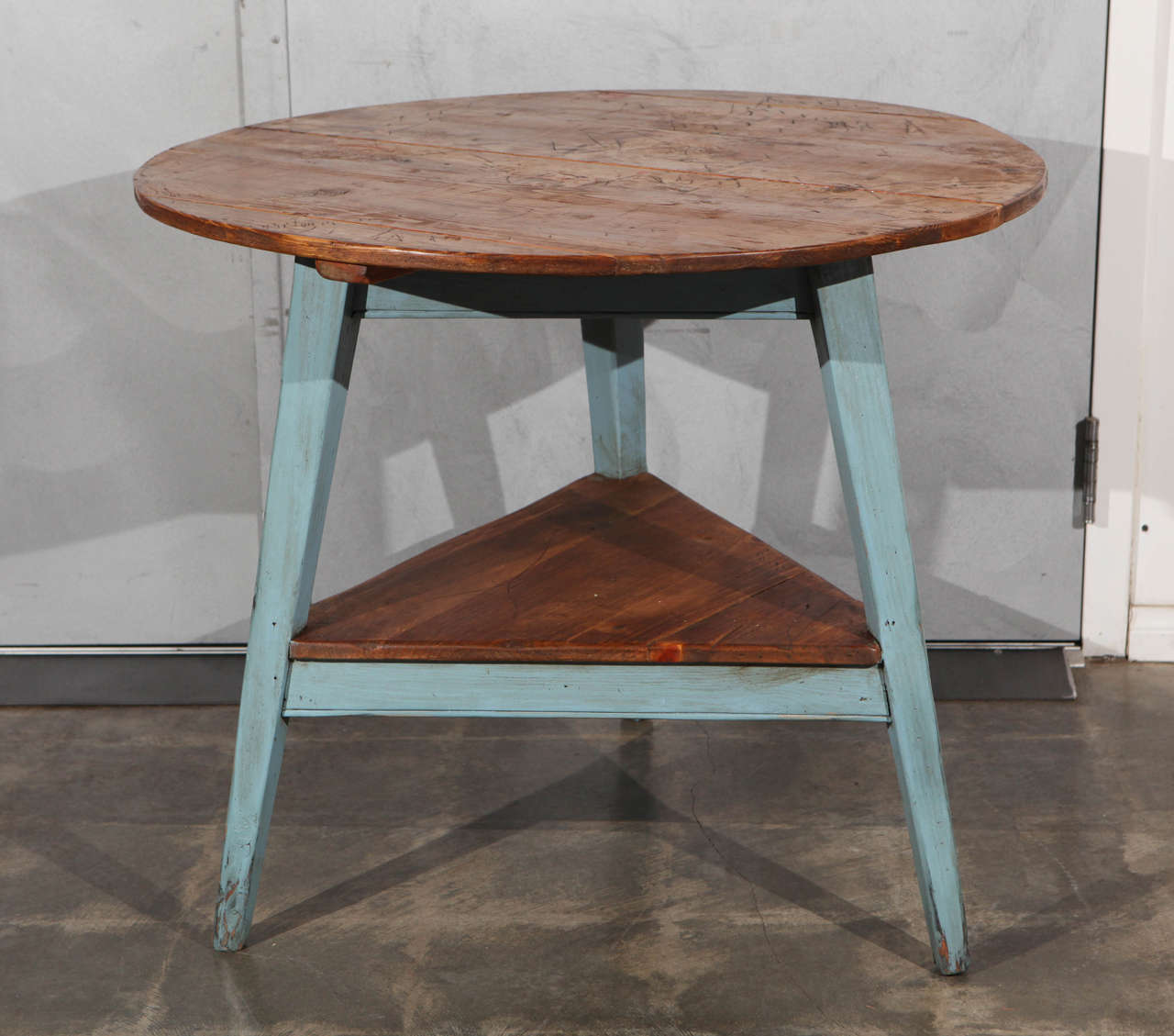 This interesting cricket table is a reconstructed piece we believe was made in England in the 1980s with an older aged wood table top and newer pine legs and triangular shelf. The blue painted legs give this piece a unique versatility for a variety