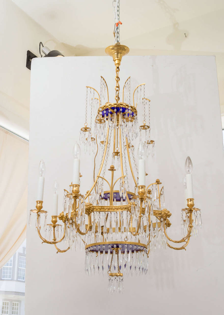 20th century French gilt bronze chandelier in the neoclassic style. Excellent very fine details of cast lions, foliage and engine turned designs. Eight arms, glass icicle type prisms and blue glass discs. Original chain and canopy.