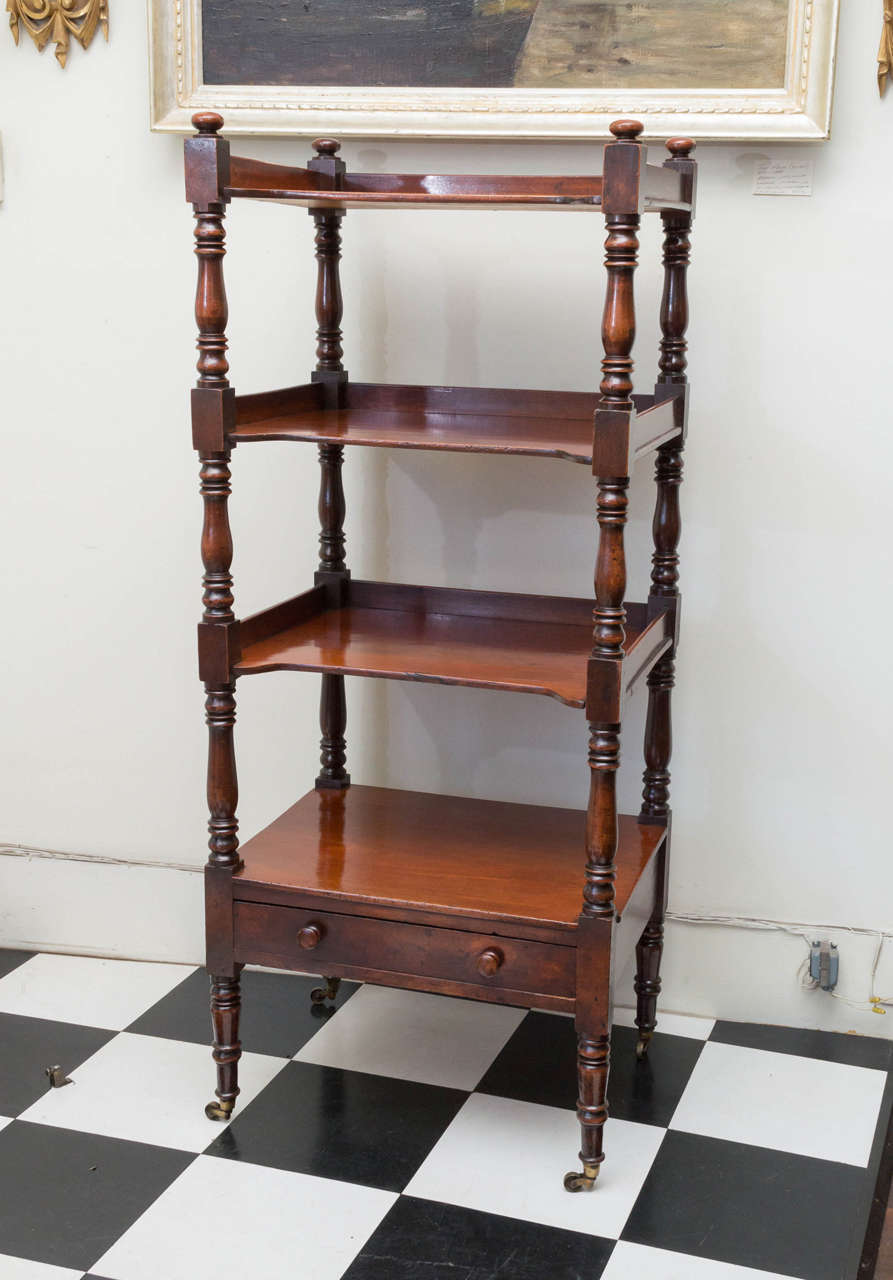19th c. English Regency mahogany etagere. Four shelves and one drawer below. With original brass casters and turned wooden drawer knobs. Excellent large scale. The top three shelves have a shaped inset to allow for easy access to the shelves below.