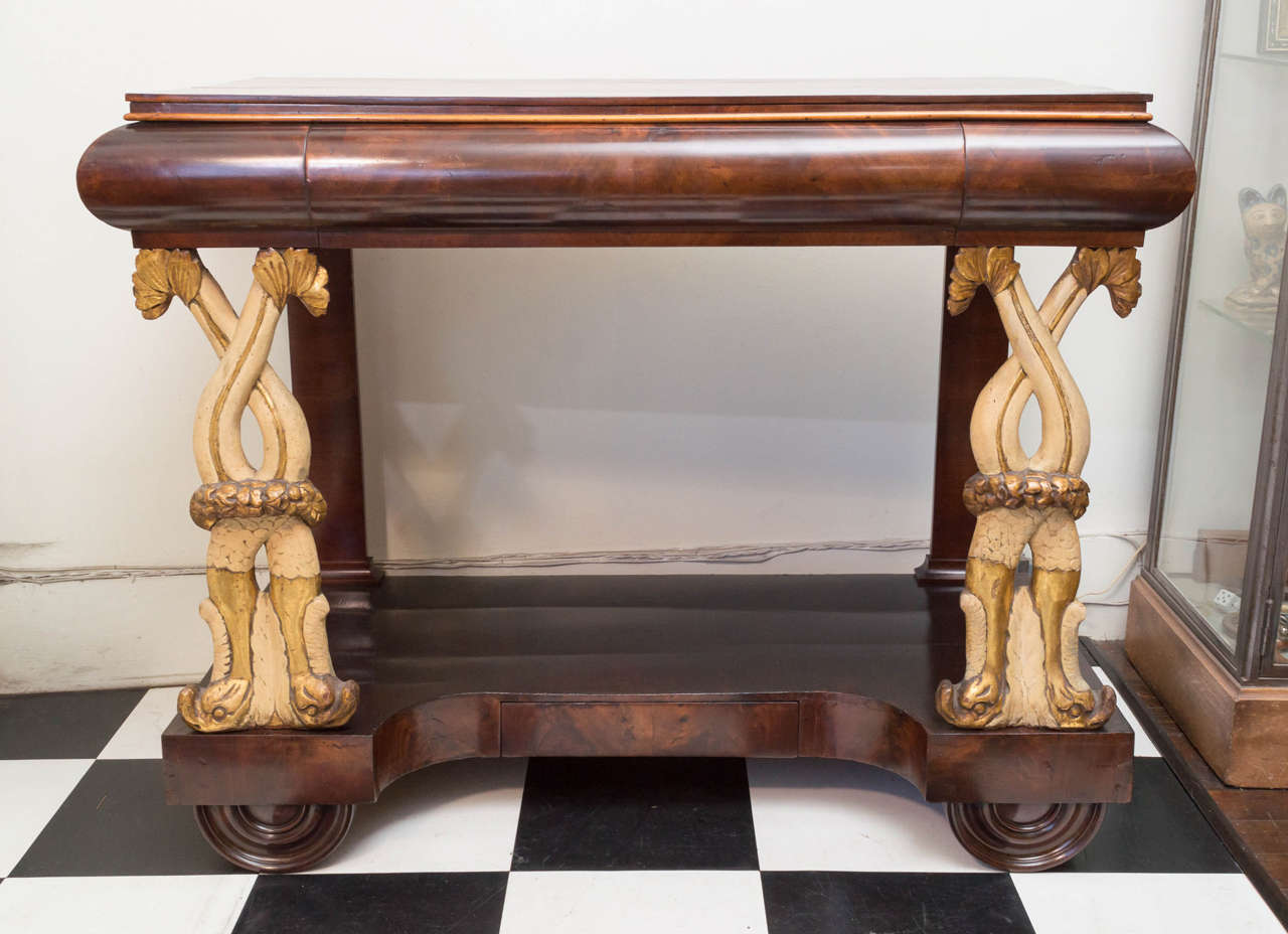 19th century Baltic mahogany large-scale console. Classic form with original carved, painted and parcel-gilt dolphin form legs. Two drawer top and a small drawer in the shelf / plinth base. Polished and refinished, circa 1825.