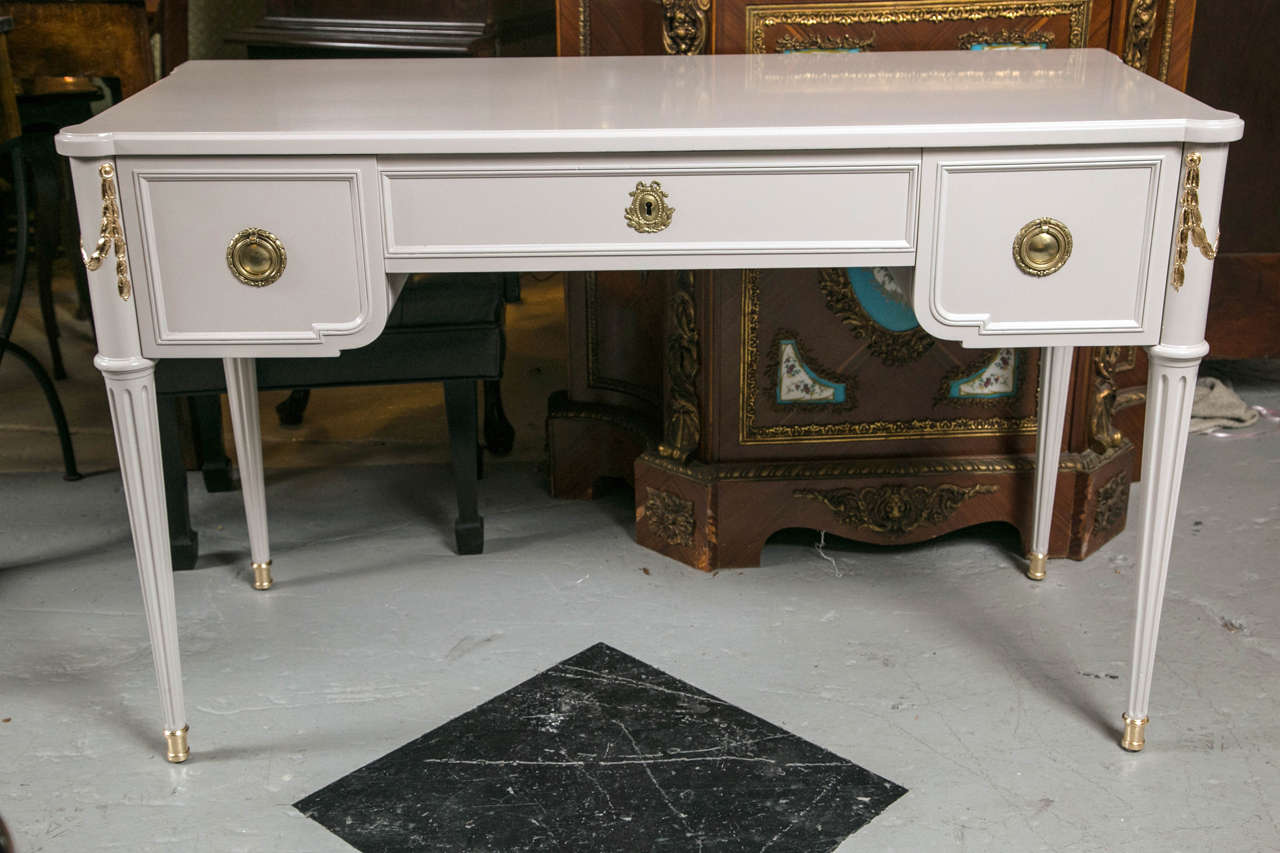 Paint decorated and gilt gold vanity or desk by John Widdicomb. This light grayish paint decorated desk in the Louis XVI style has a warmth and charm to fit into most any interior in the home or office. The tapering legs supporting a knee hole desk