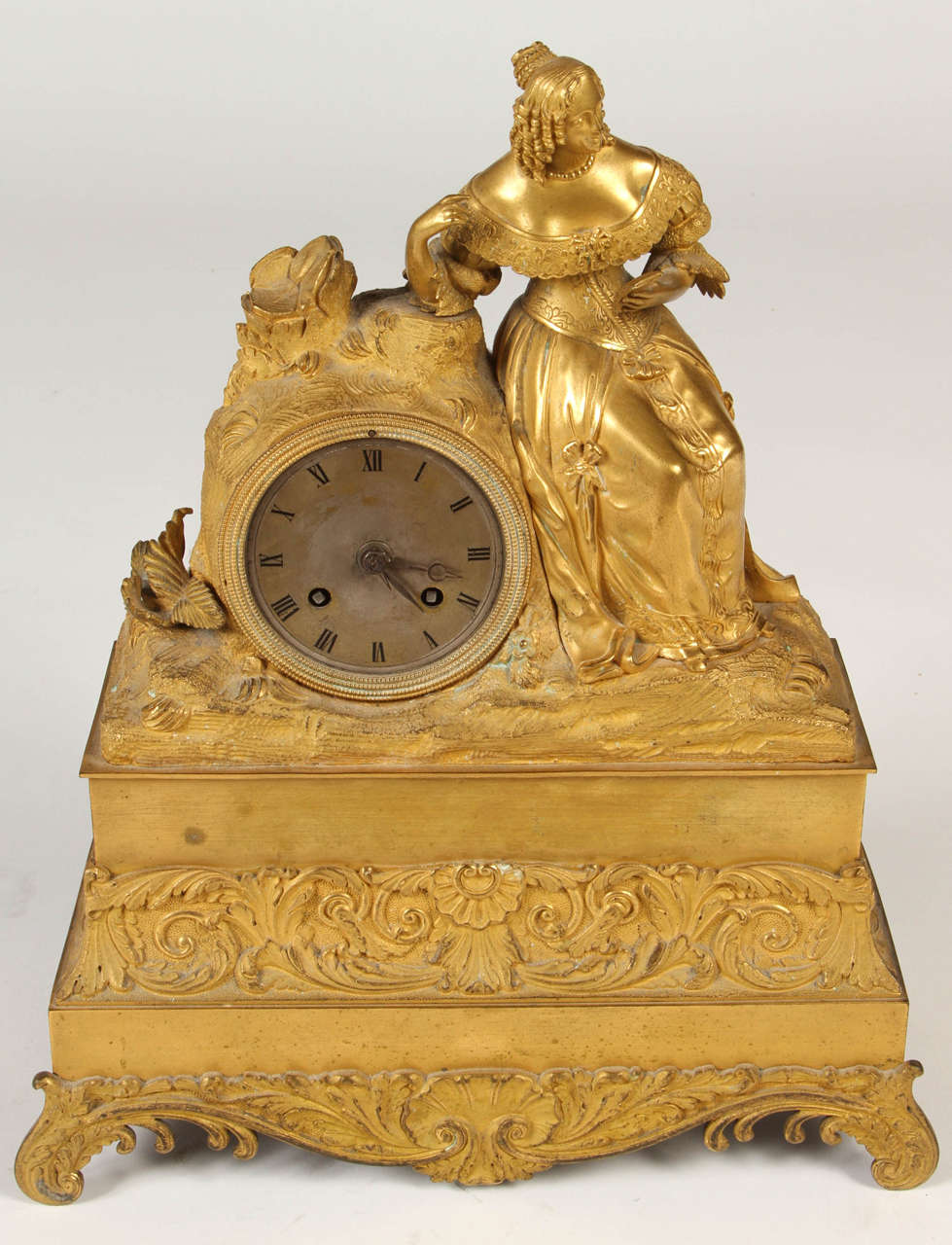 A fine French Empire mantle clock from the mid 19th century with a rectangular tiered drum case surmounted by the figure of a woman in period attire reading a book. The rectangular stepped plinth is decorated with foliage in the rococo style.

The