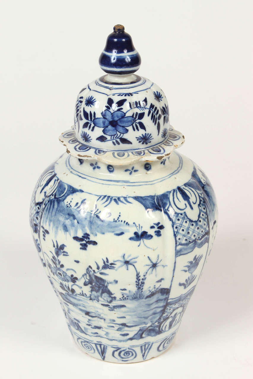Lovely Delft vase from the 18th century in blue and white with bulbous shaped finial, ribbed sides comprised of three panels decorated with flowers, trees, and figures. This vase is a wonderful example of 18th century Delft pottery.