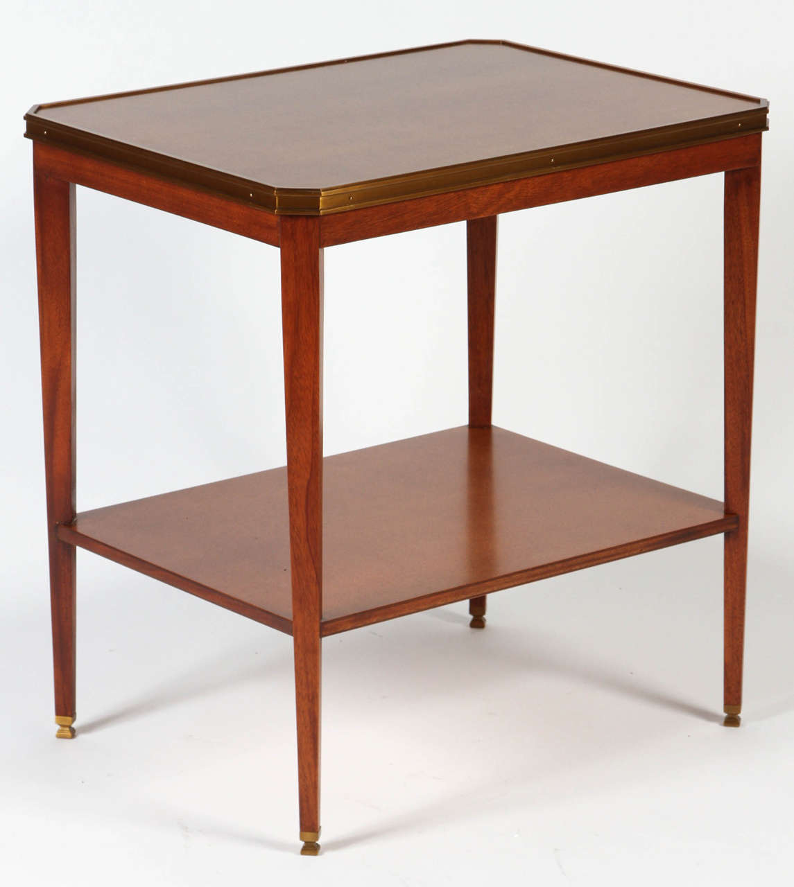 These lovely side tables are made from richly grained mahogany with an anegre wood top. They features a wood shelf and a French Brass rim surrounding the top and slender tapered posts capped with matching antique brass ferrules. Classic clean lines