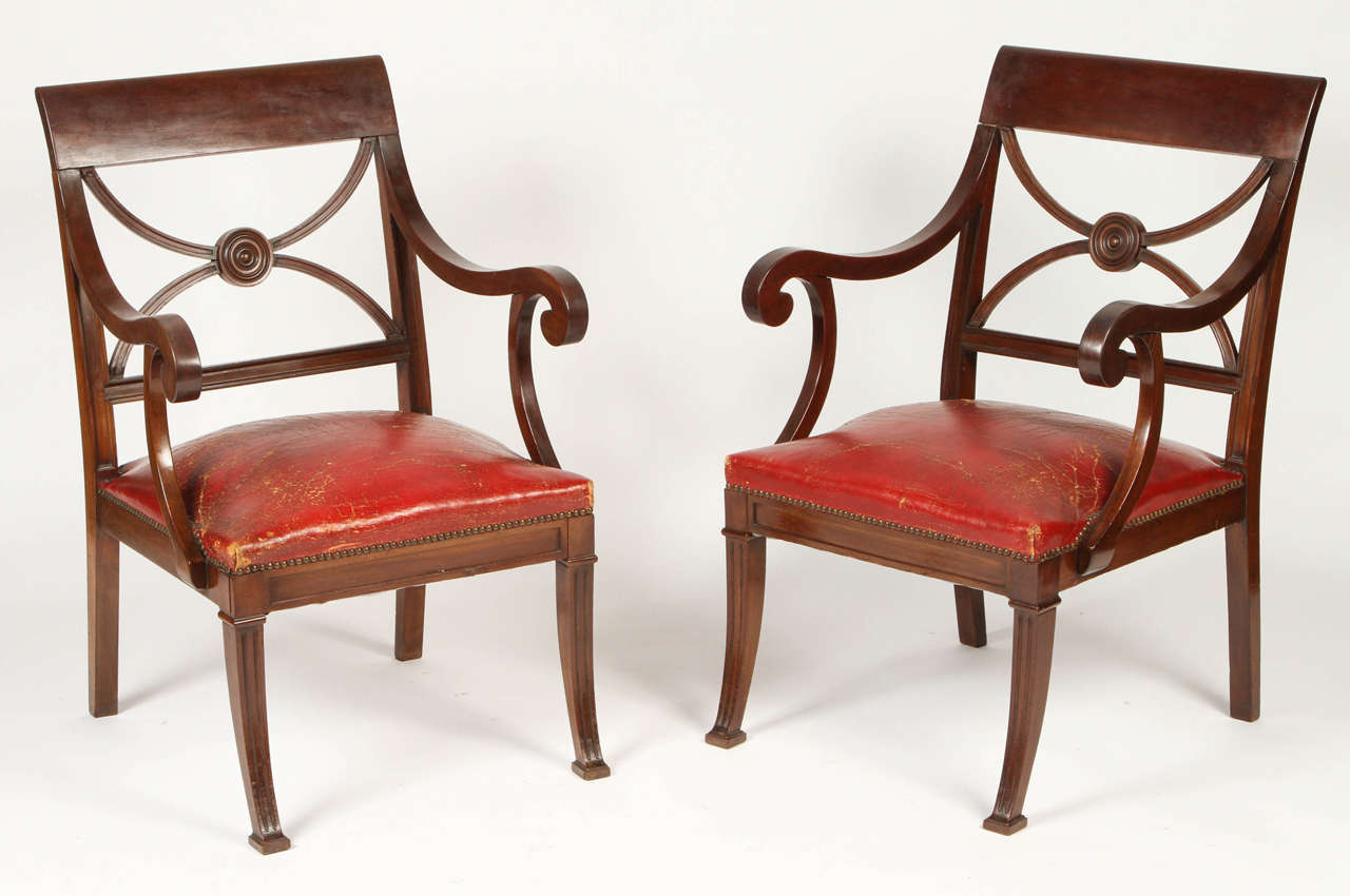 This classic pair of English Regency armchairs from the mid to late 19th century are made from warm mahogany. An X-back splat with centre medallion and down scrolled arms sit above the original red leather seats with nailhead trim. The sabre legs